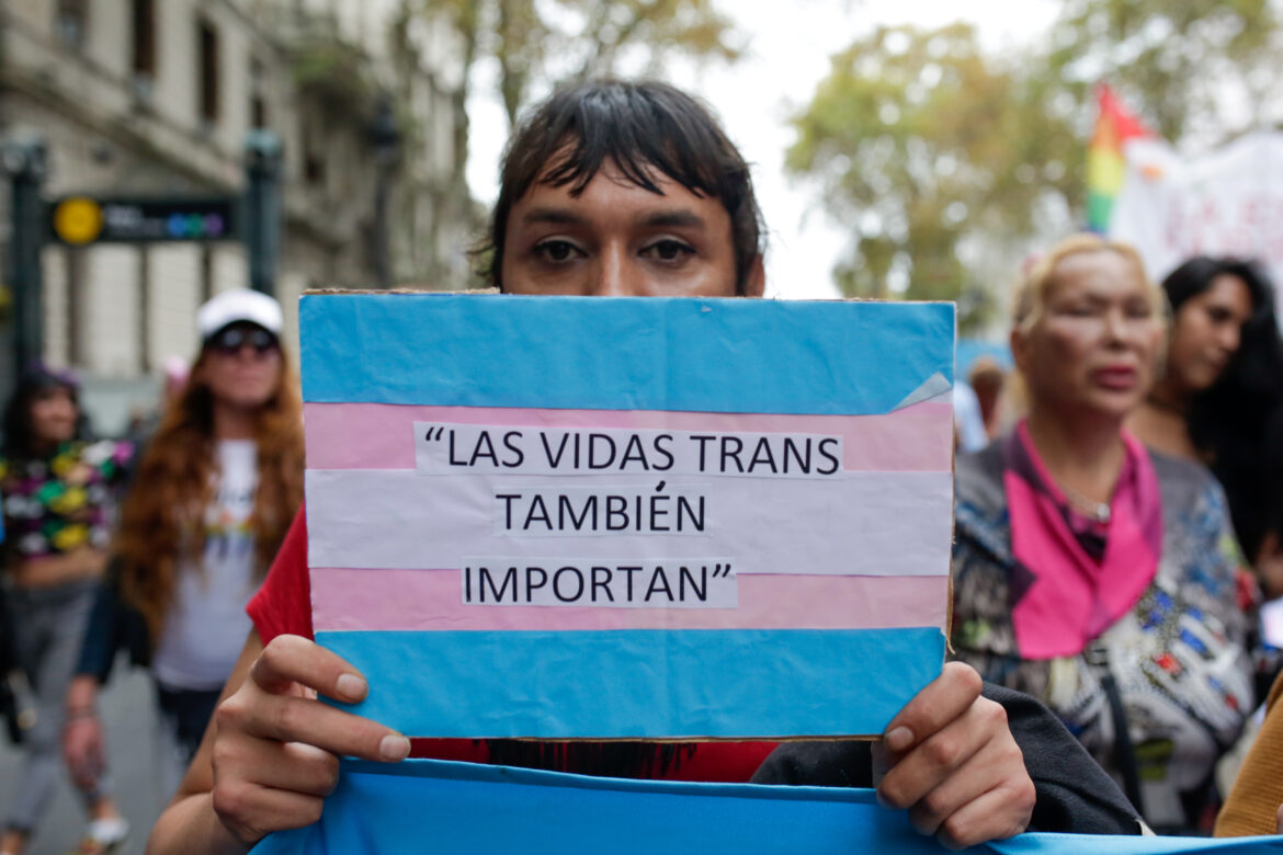 A person in the street holding a sign that says "Las vidas trans también importan" (Trans lives also matter)