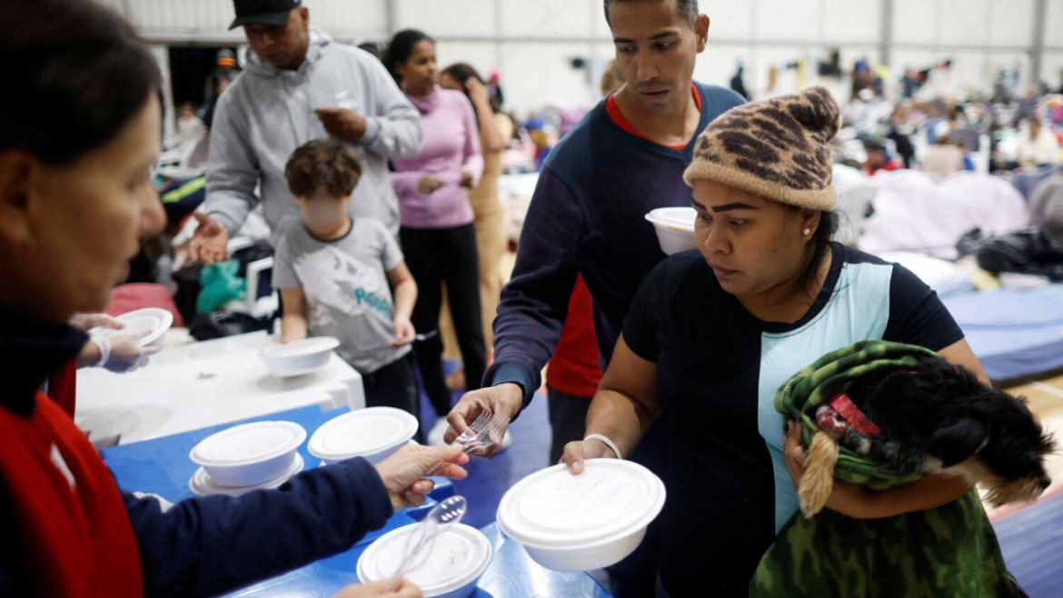 Venezuelan refugees Carina Gonzales and Xavier Velasquez receive dinner from a volunteer at a shelter after their house was destroyed by floods, in Porto Alegre, Rio Grande do Sul state, Brazil, May 14, 2024. REUTERS/Adriano Machado